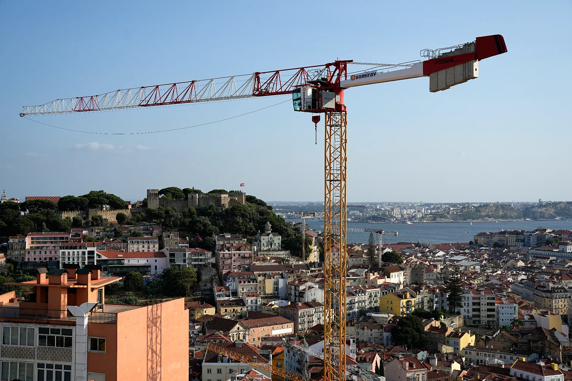 A crane rises above the buildings, with São Jorge Castle and the river Tagus in the background, in Lisbon